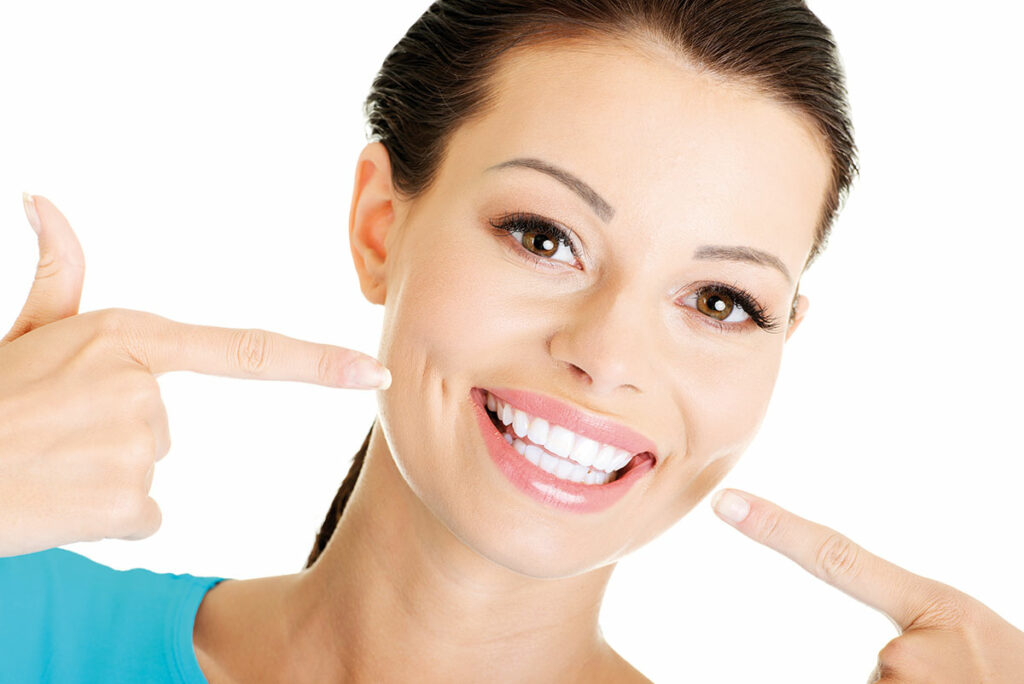 Frau lächelnd zeigt auf ihre gebleachten Zähne.