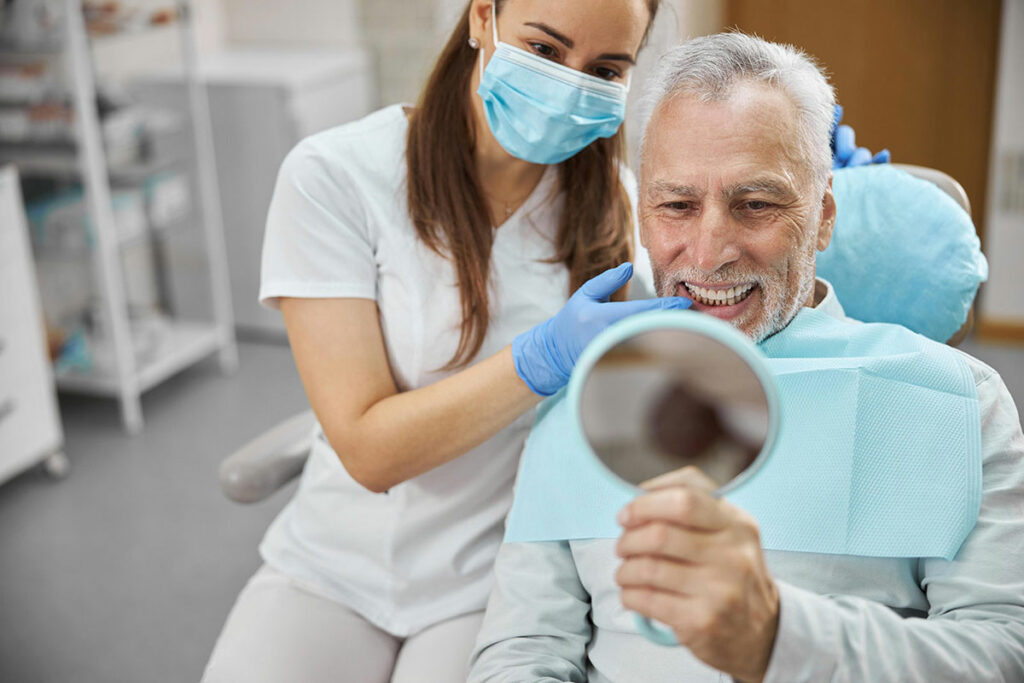 Zahnärztin zeigt Patienten seine schönen neuen Zähne über einen Spiegel